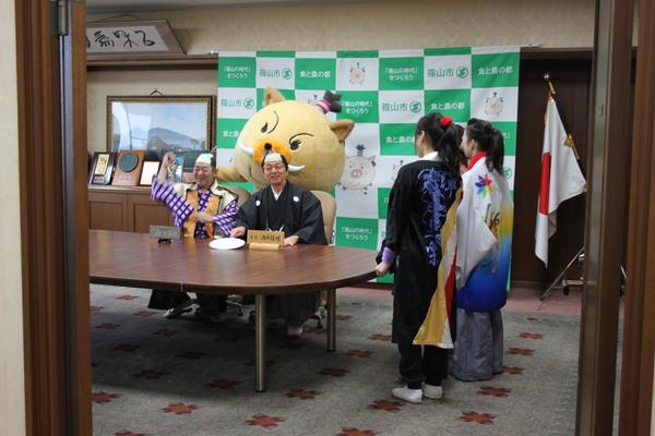 市長室に紋付袴を着てちょんまげのカツラを被った市長と議長が座っているところ、よさこい3人娘が踊りの誘いに来室した写真