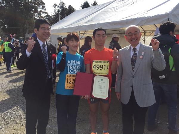 真ん中には男性ランナーと女性ランナー、はじには市長とスーツ姿の男性が並びガッツポーズをしている写真