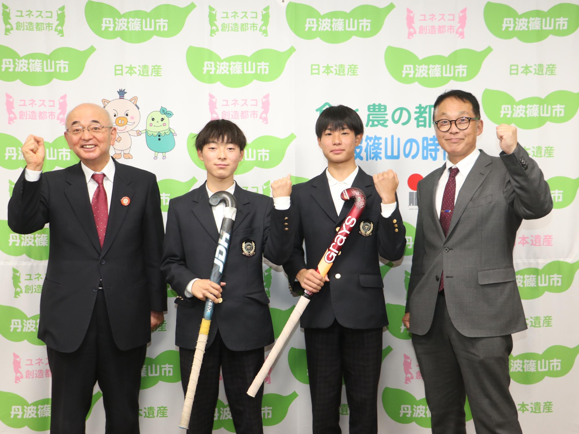 ホッケーのスティックを手に持った田中さんと中井さん、市長、教育長との記念撮影
