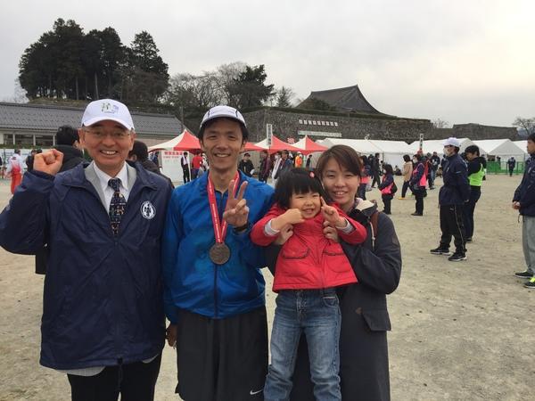 市長と、首にメダルをかけた男性、女の子を抱きかかえた女性が並んでいる写真