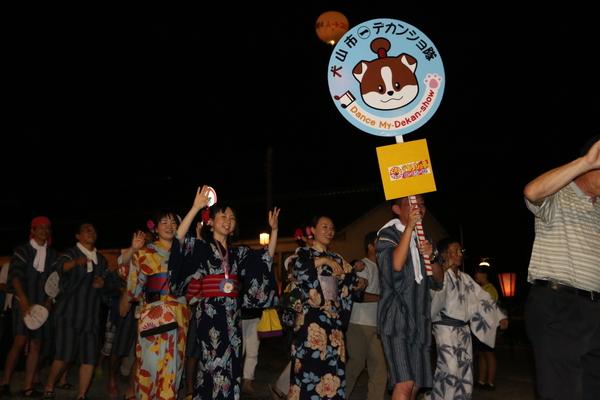 「犬山市デカンショ隊」のプラカード持った甚平姿の男性を先頭に浴衣姿で踊る人々の写真