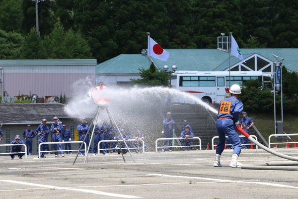 ヘルメットを着用している作業服姿の消防団員が丸いパネルに向かって放水している写真