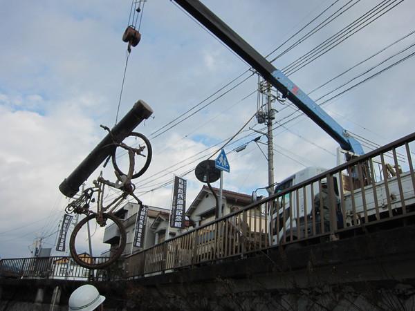 橋の上から、クレーン車で自転車を吊り下げ回収している写真