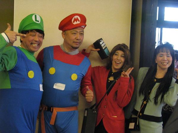 スーパーマリオのマリオとルイジ―仮装をしている男性とお笑い芸人の平野ノラのコスチュームを真似て赤と水色のボディコンスーツと携帯電話を持た女性2人が笑顔写っている写真