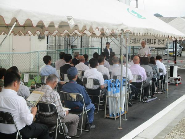 テントの中で市長が挨拶しているのを聞いている人々の写真