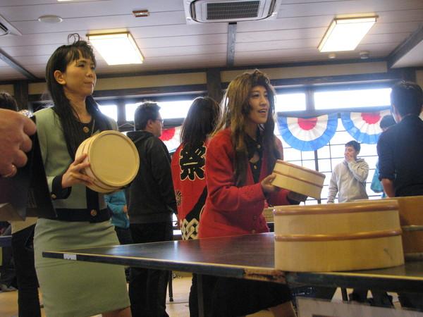 お笑い芸人 平野ノラのコスチュームを真似て赤と水色のボディコンスーツを着た女性2人が卓球台の前で、桶を持って構えている様子の写真