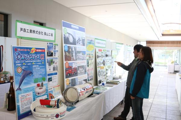 写真を使って企業が説明しているパネルを見ながら、興味を持って見ている男性と女性が写っている写真