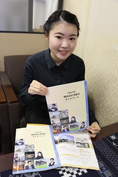 女性が「篠山市企業紹介ガイドブッック」を手に持ち表紙を見せて紹介している写真