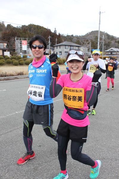 丹波篠山ふるさと大使の熊谷 奈美さんがサングラスをかけて走っている選手と一緒にガッツポーズしている写真
