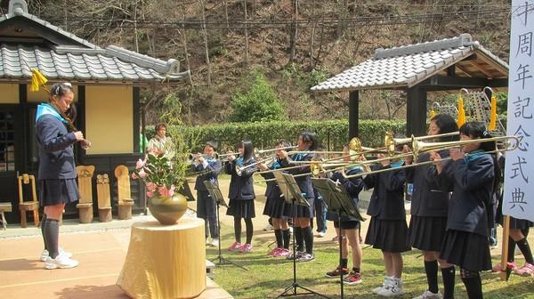 指揮棒を持った女子学生が立っていて、その前で吹奏楽の8名の女子学生がトロンボーンを演奏している写真