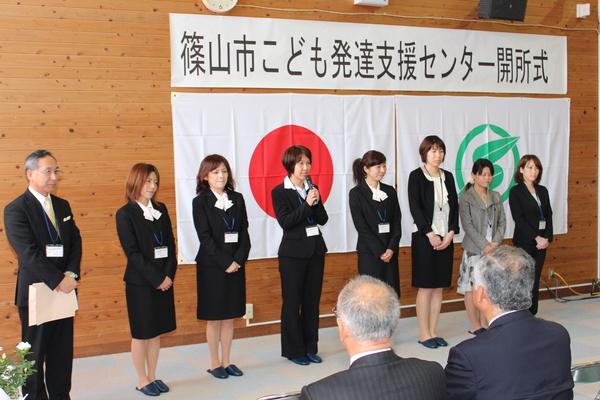 こども発達支援センター開所式でスーツを着た8人が並び、女性が挨拶をしている写真
