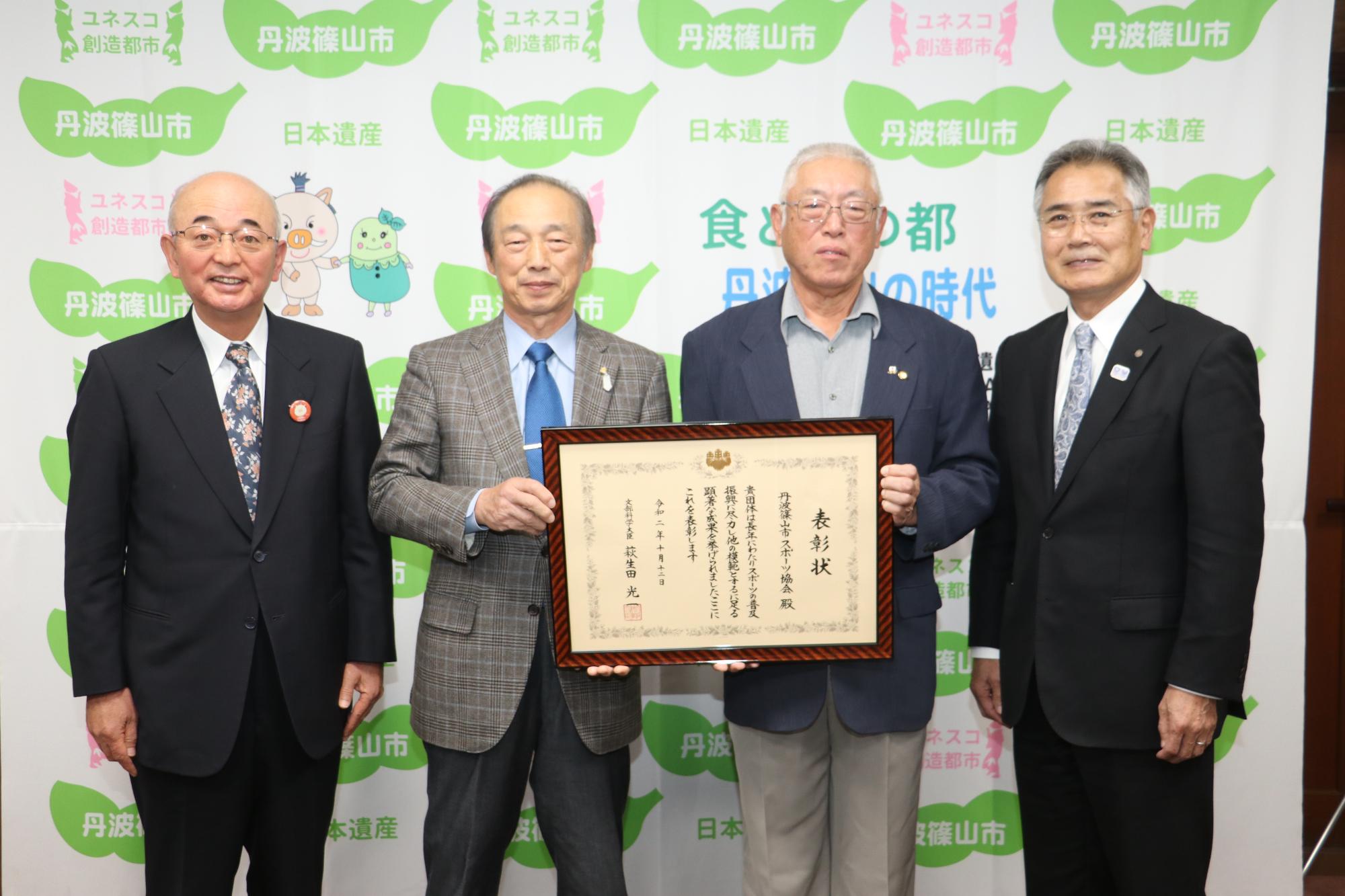 額縁に入った表彰状を持っているスポーツ協会の方、その隣に酒井市長と前川教育長