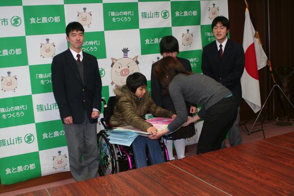 車いすに乗った女子生徒からカレンダーを受け取っている女性の写真