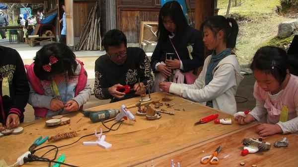 5名ほどの子供たちが男性に教えてもらいながら、どんぐりや松ぼっくりを使って工作をしている写真