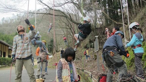 木から吊るされたロープをヘルメットをかぶった5名ほどの子供たちが登っている写真