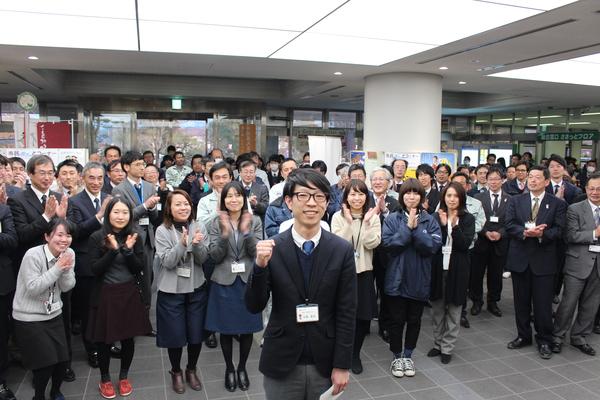 中森恵佑君がガッツポーズを決め、後ろに大勢の職員が拍手している写真