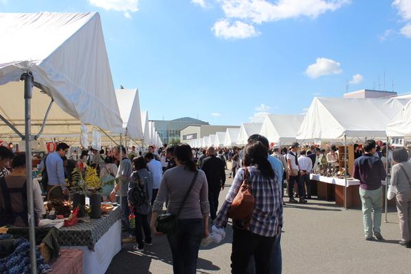 たくさんのテントがあり立ち止まって見る人々や歩く人々の写真