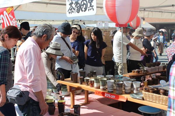 テントの中に並べられている陶器を見ている人々の写真