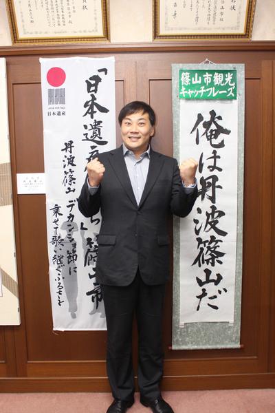 田中 美央さんが篠山市観光キャッチフレーズの前で肩の位置でガッツポーズをして記念撮影している写真