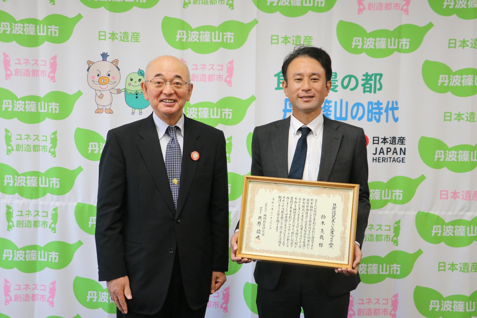 額に入った表彰状を手にしている鈴木さん、その隣に酒井市長が立っている