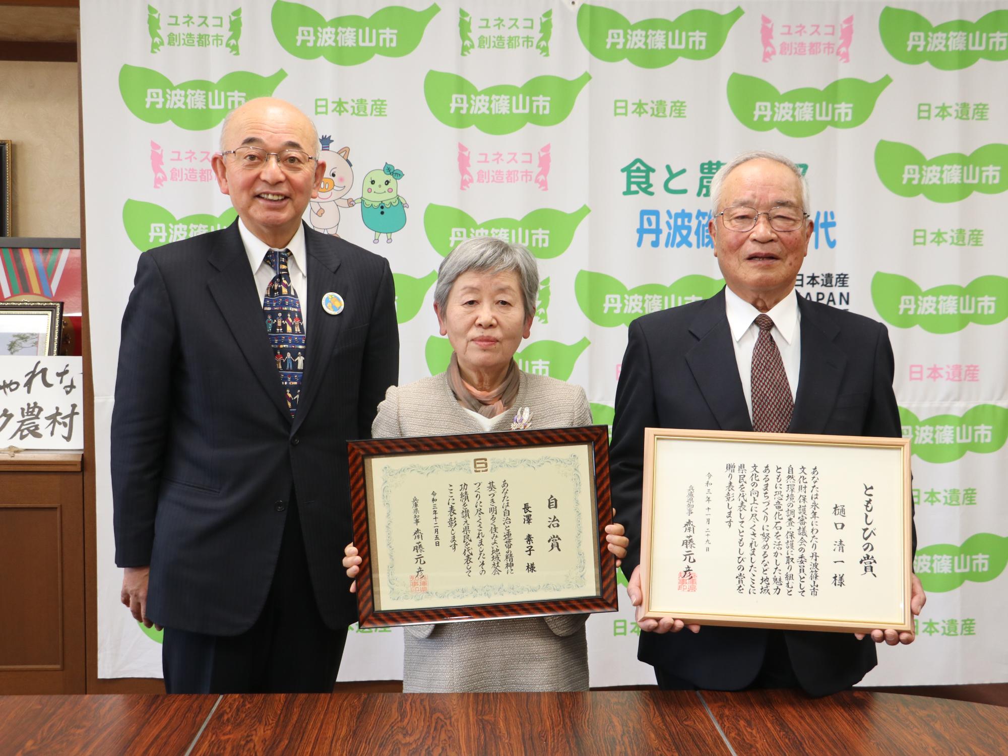額縁に入った表彰状を手にもった受賞者二人と市長の記念撮影