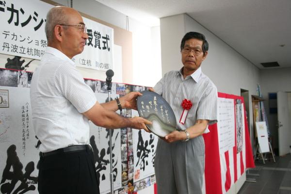 日本デカンショ節大賞授賞式にて大賞の尾川さんが、市長からまるいプレートを受け取っている写真