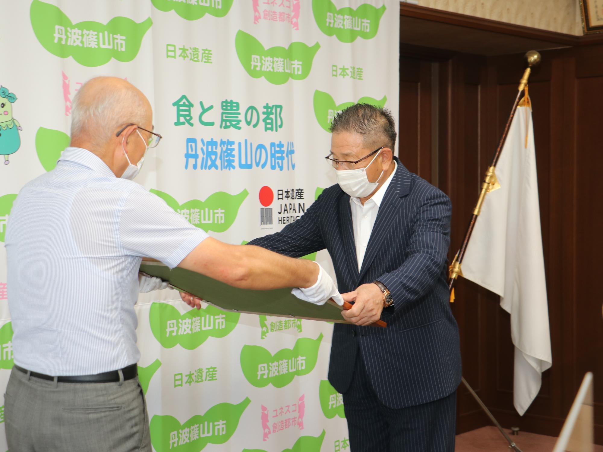 市長が白い手袋をして、紺綬褒章を男性に渡されている