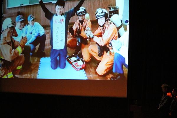 消防署チームの応援ビデオが壇上のスクリーンに映し出されている様子