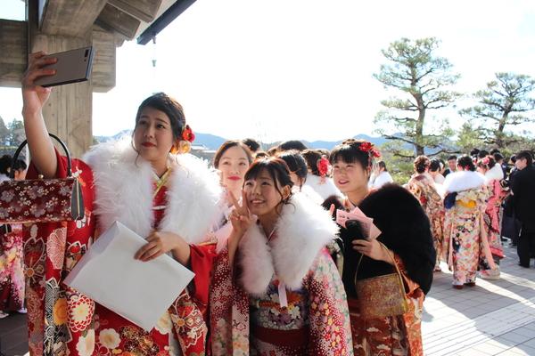 振袖を着た新成人達が自撮り写真を撮る為にスマートフォンに向かってピースサインや笑顔を向けている写真