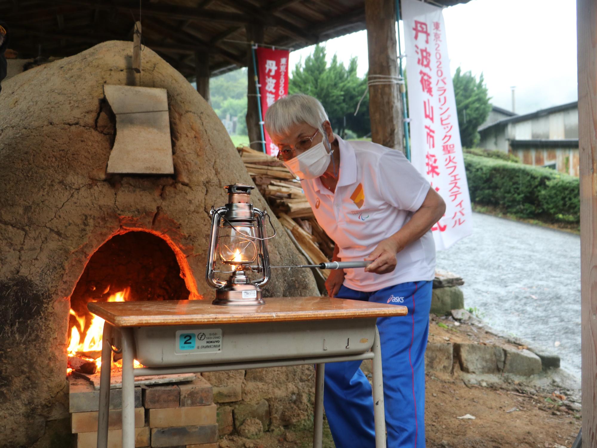 女性が登窯から聖火の火をランタンに採火している