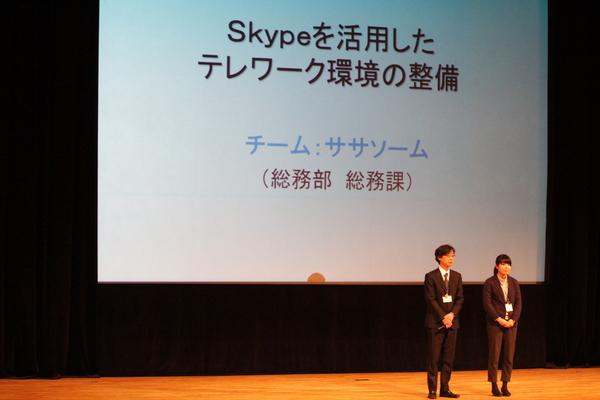 総務課チーム2名が壇上に上がっている写真・改善事例は「Skypeを活用したテレワーク環境の整備」