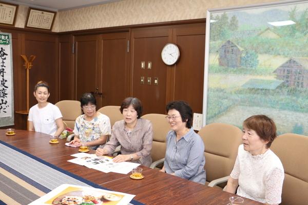 女性5人が座り、中央の女性が資料を手元に話をしている写真