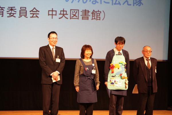 グランプリ「図書館チーム」4名が笑顔で壇上に並んでいる様子