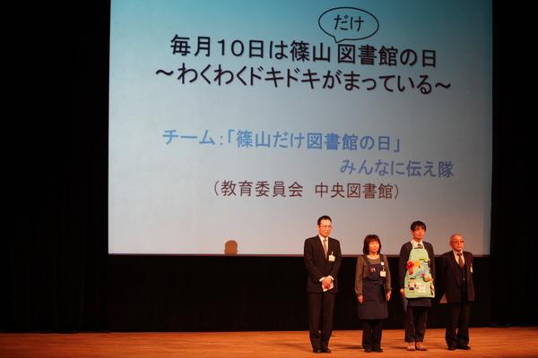 グランプリ「図書館チーム」4名が壇上に並んでいる様子・改善事例は「毎月10日は篠山だけ図書館の日」