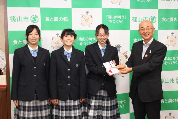 稲元さん、尾崎さん、宮本さんが並んでおり代表で宮本さんが市長と目録を持っている写真