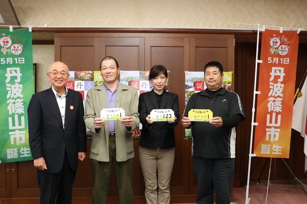 市長、石田さん、穴瀬さん、太治さんがナンバープレートを手に持って記念撮影している写真