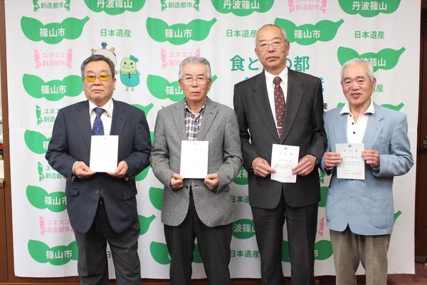 鳥獣被害対策実施隊員の松本さん、円増さん、酒井さん、細見さんが任命証を持って記念撮影している写真