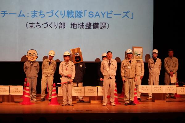 地域整備課チーム10名がヘルメットに作業着姿で壇上に上がっている写真