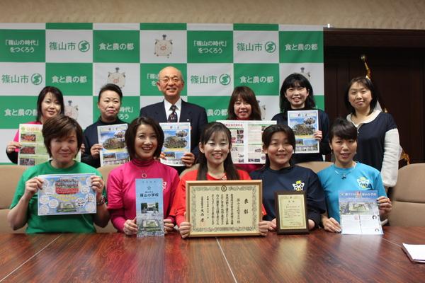 表彰状やパンフレットを持ち、市長を中央に2列に並んでいる女性たちの集合写真