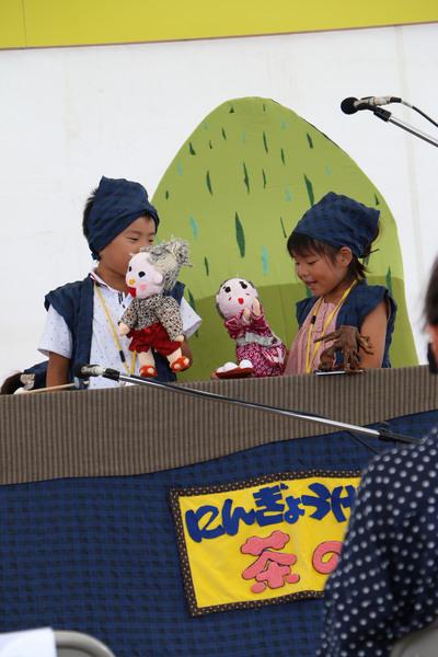 青いバンダナを頭に巻いて、青いベストを着ている男の子と女の子が指人形を付けて、人形劇を披露している様子の写真