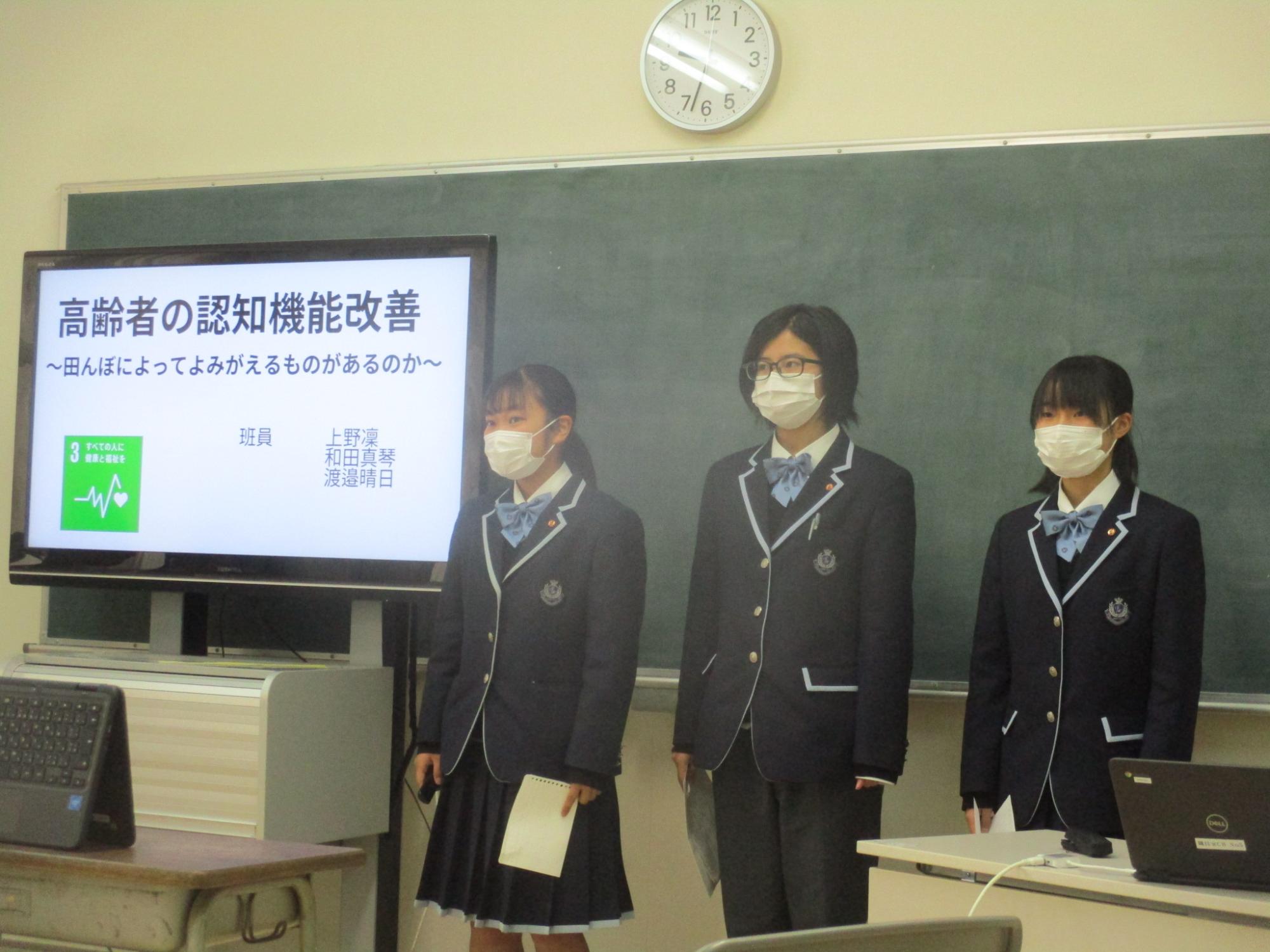 モニターの隣に女子高生2人が立って発表している