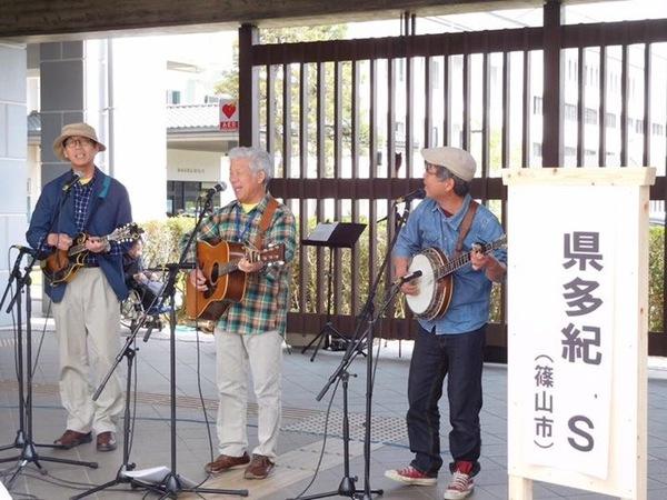 色々な形のギターを持った男性3名が歌っている写真