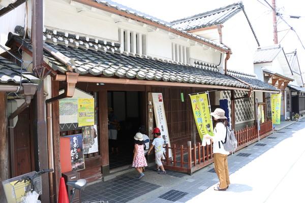 「人形劇フェスタ」ののぼりが通りの軒先に置かれており、人形劇が行なわれている家に親子連れのお客さんが入ろうとしている様子の写真