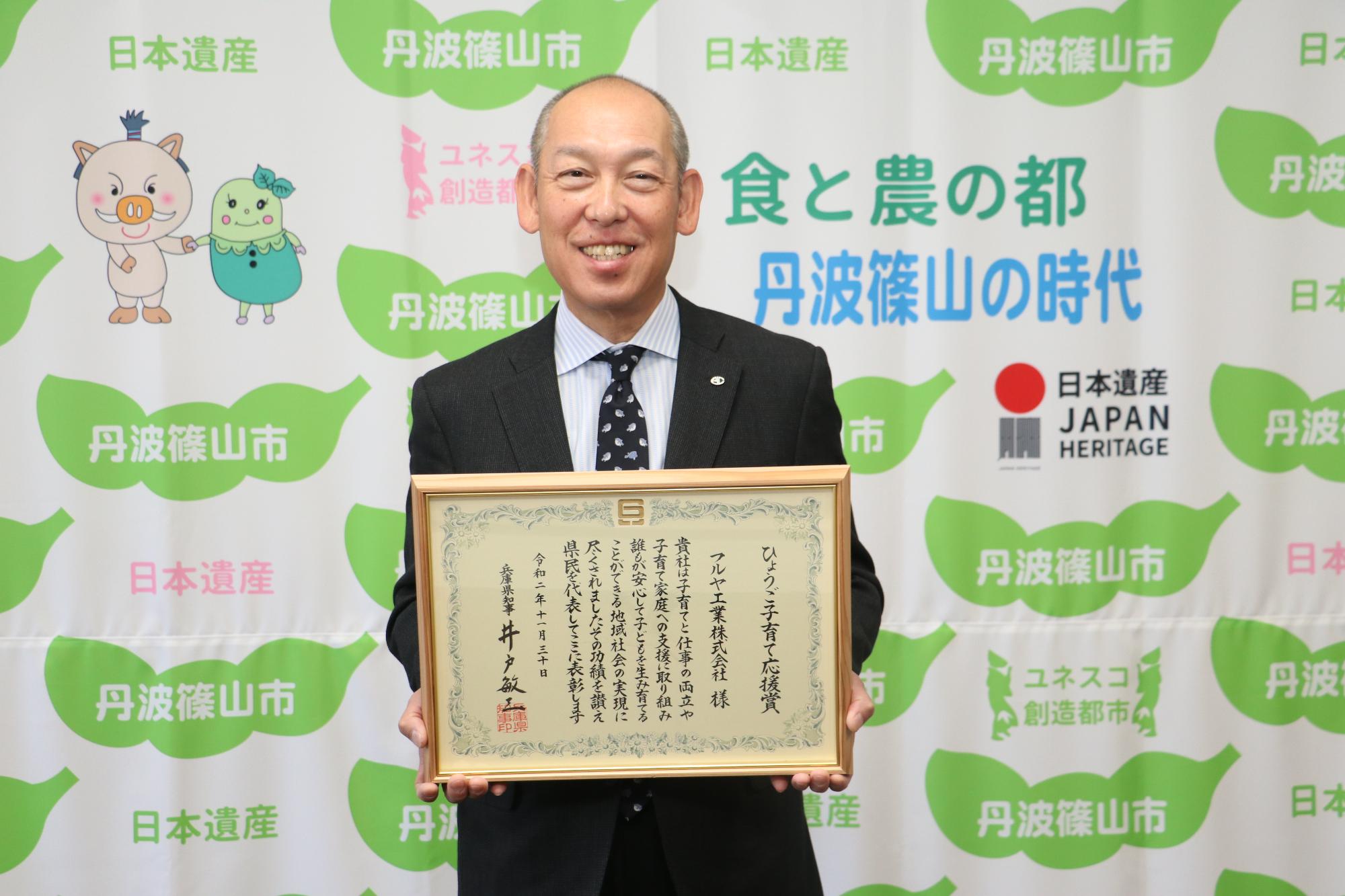 表彰状を手に、笑顔の降矢氏