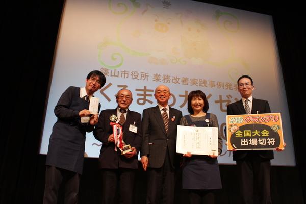 くろまめカイゼングランプリ受賞の「図書館チーム」が目録、トロフィー、賞状、全国大会出場切符のパネルを持って市長を真ん中に記念撮影