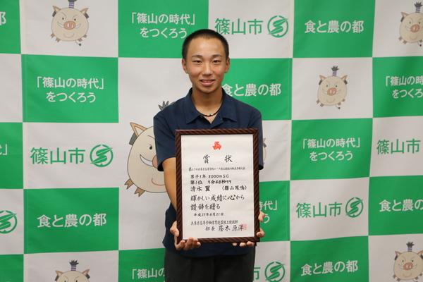 清水君が額縁に入った賞状を持って写っている写真