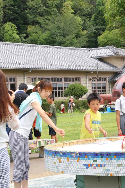 女性と少年がシャボン玉の液に棒を付けている写真