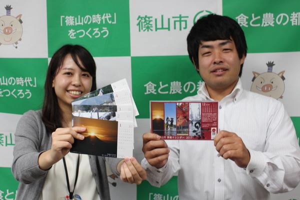 女性と男性が笑顔で、卓上型景観カレンダーを持っている写真