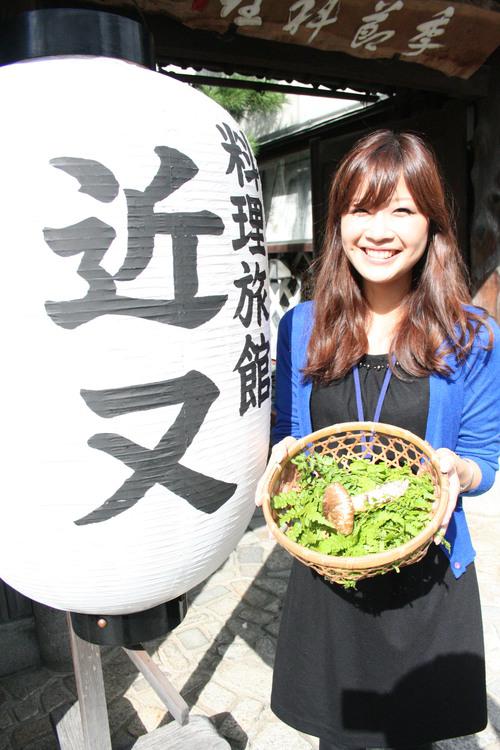 老舗料理旅館の提灯の前で、籠に入った丹波まつたけを手にニッコリ笑顔の女性の写真