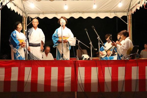 舞台の上で着物を着た女性が三味線に合わせて歌っている写真